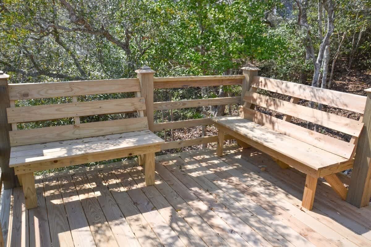 Two wooden benches on a wooden deck with a natural backdrop of trees.