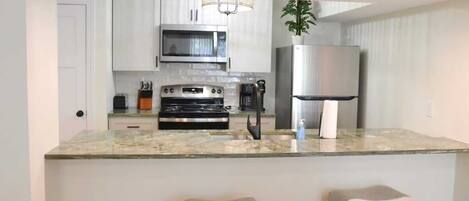 A modern kitchen with a central island, stainless steel appliances, and a hanging light fixture.