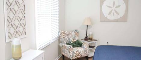 Un dormitorio con cama, una silla, una lámpara, un adorno en la pared y un armario.