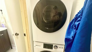 Een compacte wasmachine en droger in een kleine wasruimte met een houten vloer en een blauwe handdoek in de buurt.