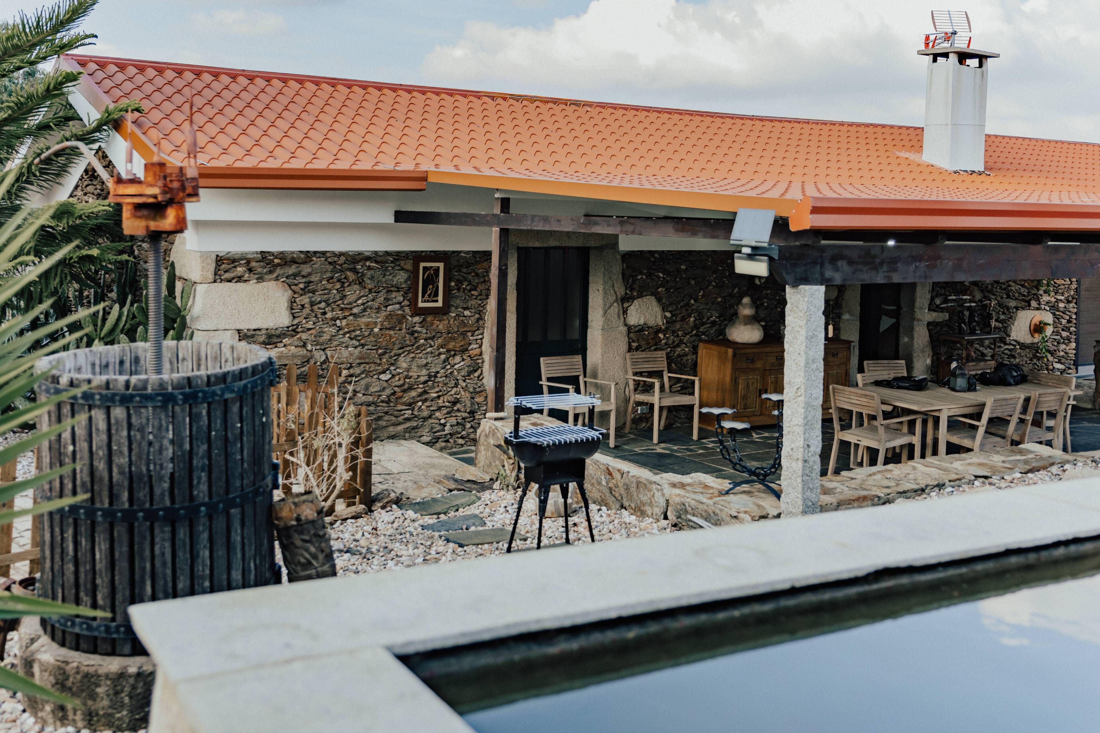 Une maison avec un toit recouvert de tuiles rouges, des murs en pierre, un espace barbecue et une piscine.