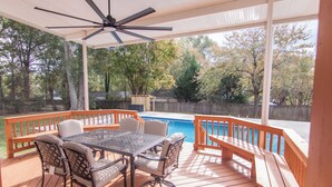 Eine überdachte Terrasse im Freien mit Pool, Holzmöbeln und Deckenventilator.