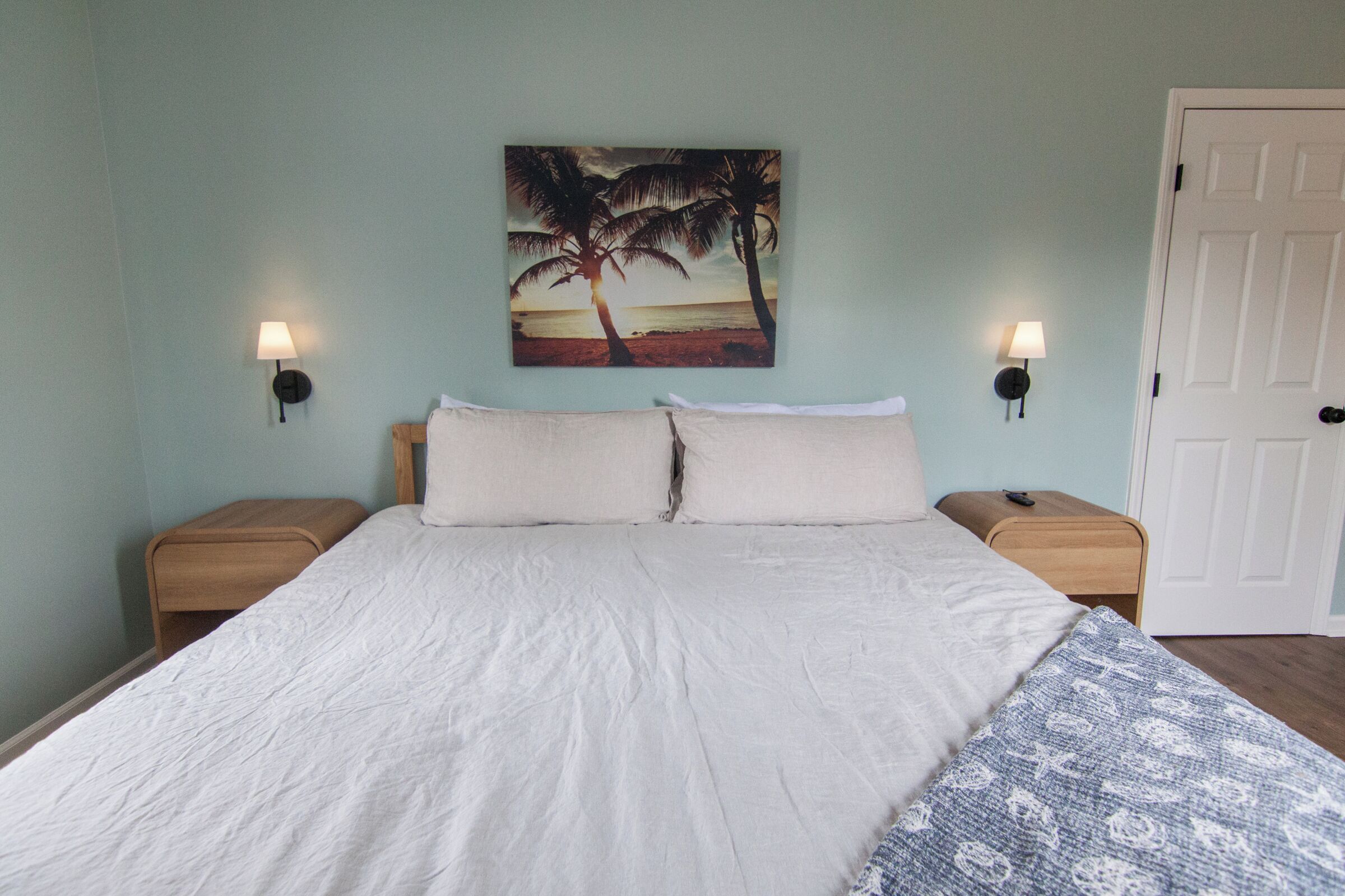 A bedroom with a bed, two nightstands, a wall-mounted lamp, and a door.