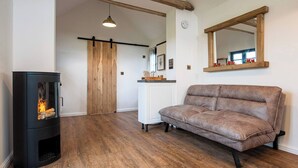 A room with a wood-burning stove, a sofa, a wooden-framed mirror, and a sliding barn door.