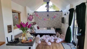 A room with a bed, a desk with a computer, a window with curtains, and a brick wall.