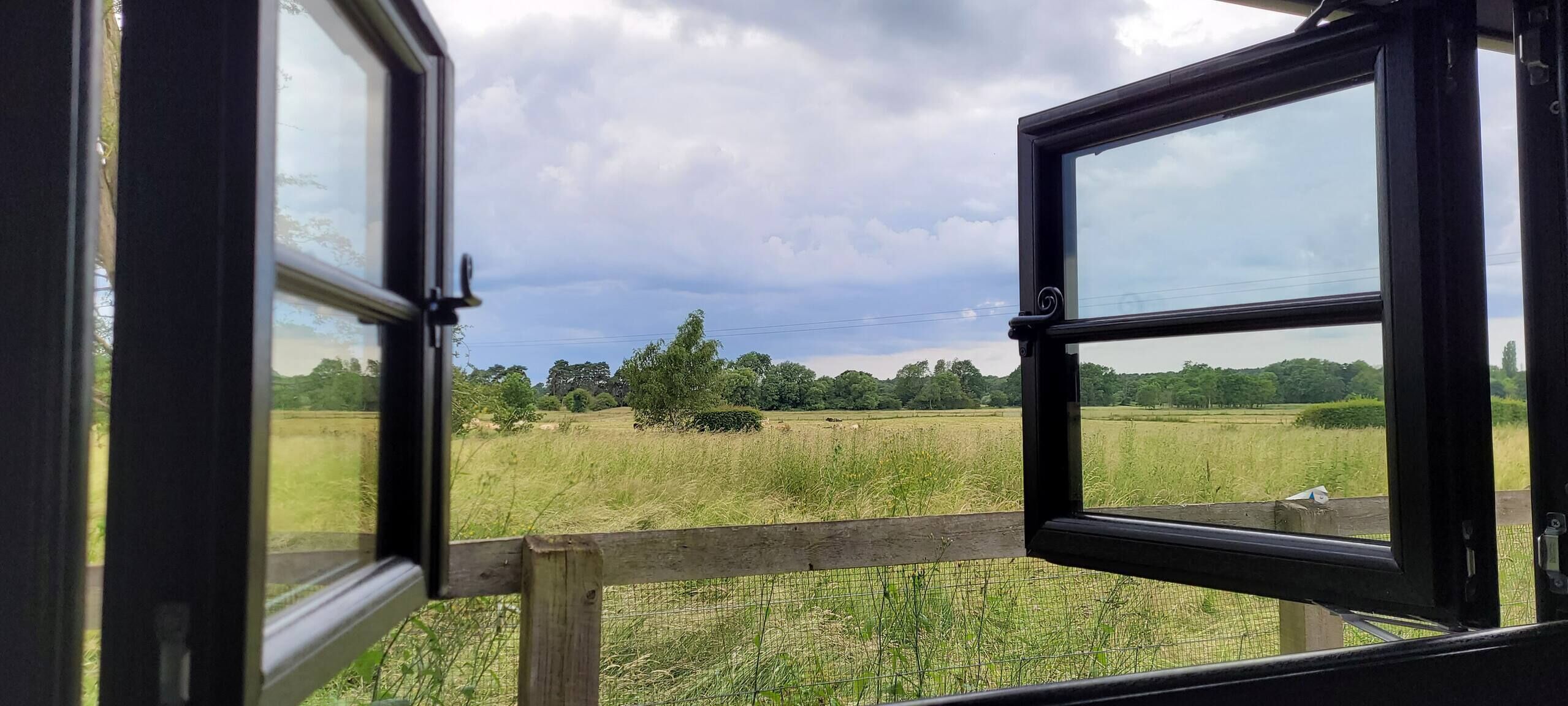 Blick durch offene Fenster auf eine ländliche Landschaft mit Feldern und Bäumen.