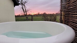 A hot tub with a view of a sunset over a grassy field.