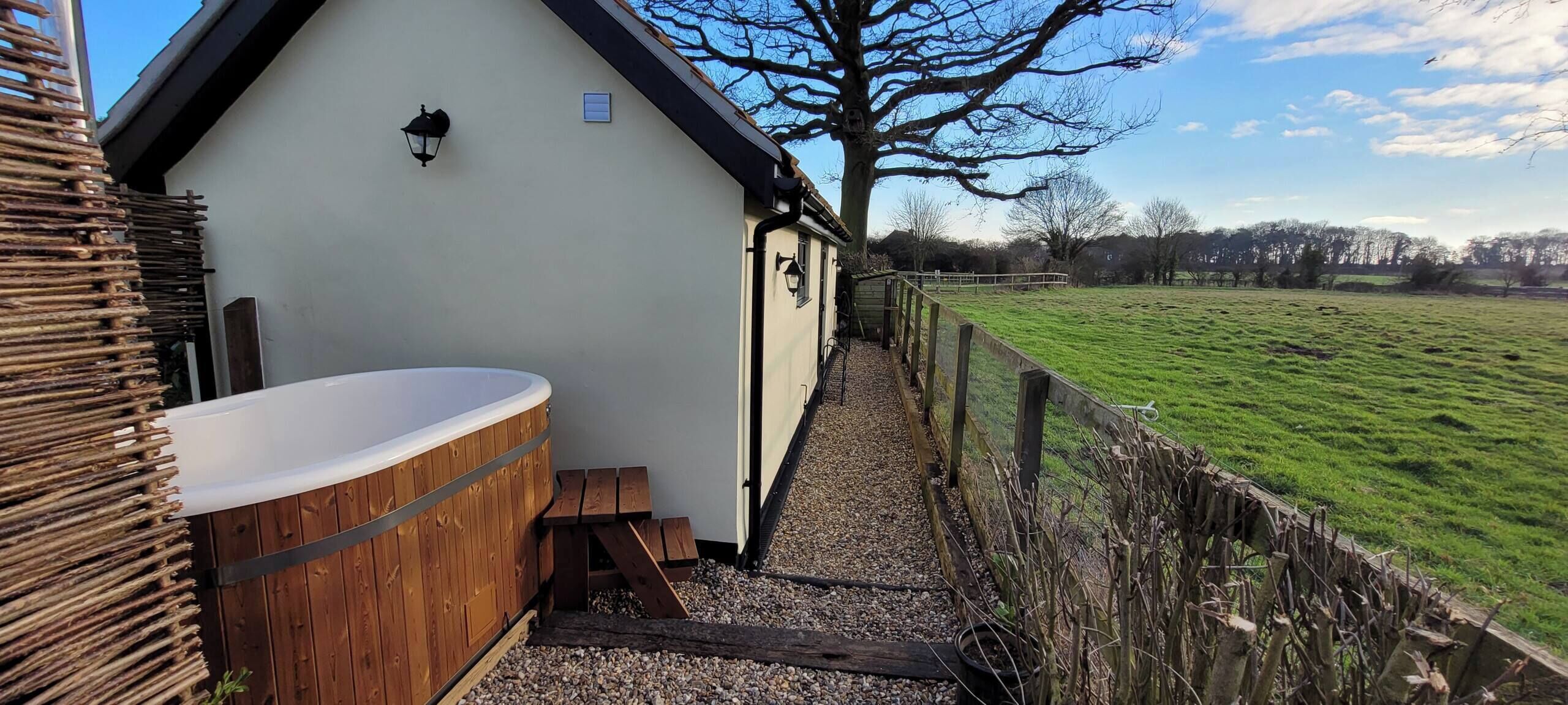 A spa area with a hot tub, wooden steps, and a view of a green field.