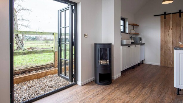 A kitchen with a sliding glass door leading to a gravel area, a wood-burning stove, and a hanging pendant light.