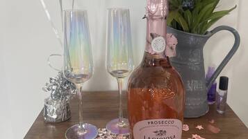 A bottle of Prosecco, two glasses, a decorative plant, and scattered confetti on a wooden surface.