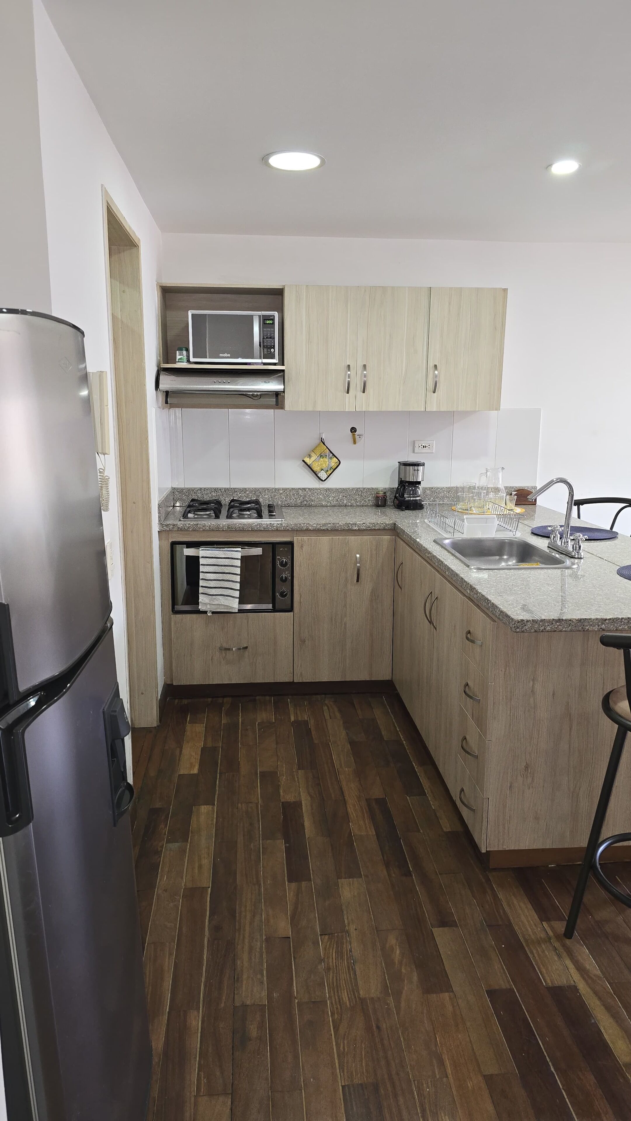 Eine moderne Küche mit Holzschränken, einem Edelstahlkühlschrank, einer Mikrowelle, einem Herd und einem Spülbecken.