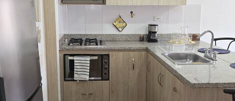 Una cocina moderna con armarios de madera, un refrigerador de acero inoxidable, un microondas, una estufa y un lavamanos.