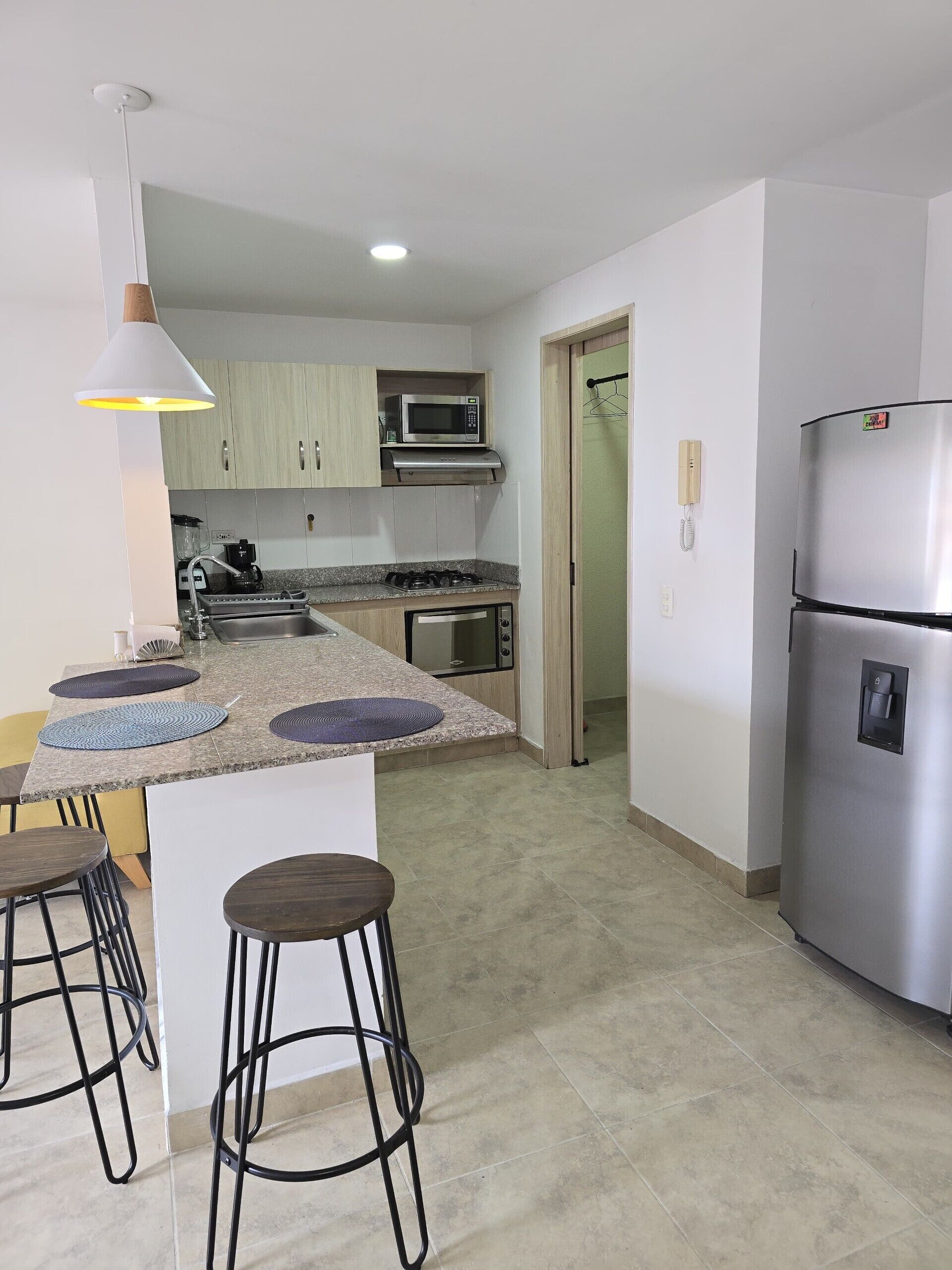 A modern kitchen with a central island, bar stools, a refrigerator, and a microwave.