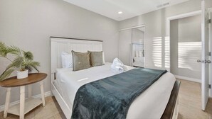 A hotel room with a bed, a small table with a plant, a mirror, and a door. - 10 Min to Mission Beach & Sea World | Kids Playset (San Diego)