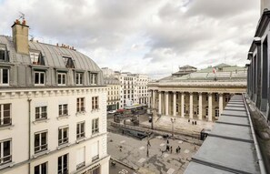 Blick auf einen Stadtplatz mit historischen Gebäuden, darunter ein großes neoklassizistisches Bauwerk mit Säulen.