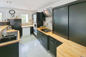 Una cucina moderna con mobili neri, un piano di lavoro in legno, forno integrato e cappa aspirante in acciaio inossidabile.