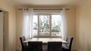 Quarto com mesa de jantar e cadeiras, janela com cortinas e vista para o exterior.