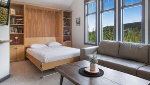 Een slaapkamer met een bed, een slaapbank, een houten tafel en een boekenkast.