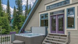 Een hottub op een houten terras, een paarse deur en uitzicht op bomen.