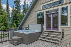 Ein Whirlpool auf einer Holzterrasse, eine violette Tür und Blick auf Bäume.