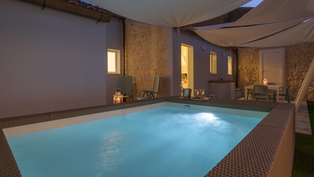 Ein Schwimmbecken mit gefliestem Rand, umgeben von Liegestühlen und einer überdachten Terrasse.
