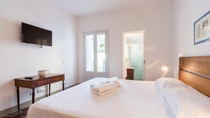 Ein Schlafzimmer mit einem Bett, einem an der Wand montierten Fernseher, einem Schreibtisch mit einer Schale und einer Tür zu einem weiteren Raum.
