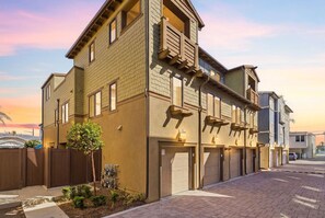 A multi-story residential building with a brick facade, multiple garage doors, and a small tree in the front yard. - Modern Beach Townhome: Steps to Ocean, Bay & Belmont Park (San Diego)
