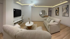 Ein modernes Wohnzimmer mit Flachbildfernseher, zwei Sofas, einem Couchtisch und einem Spiegel.