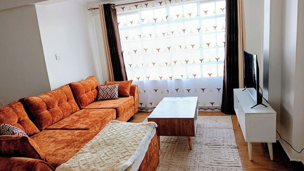 Ein Wohnzimmer mit Sofa, Couchtisch, TV-Schrank und Vorhängen mit Muster.