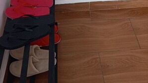 Eine Raumecke mit Holzboden, einem schwarzen Metallregal und Flip-Flops sowie einer weißen Wand.