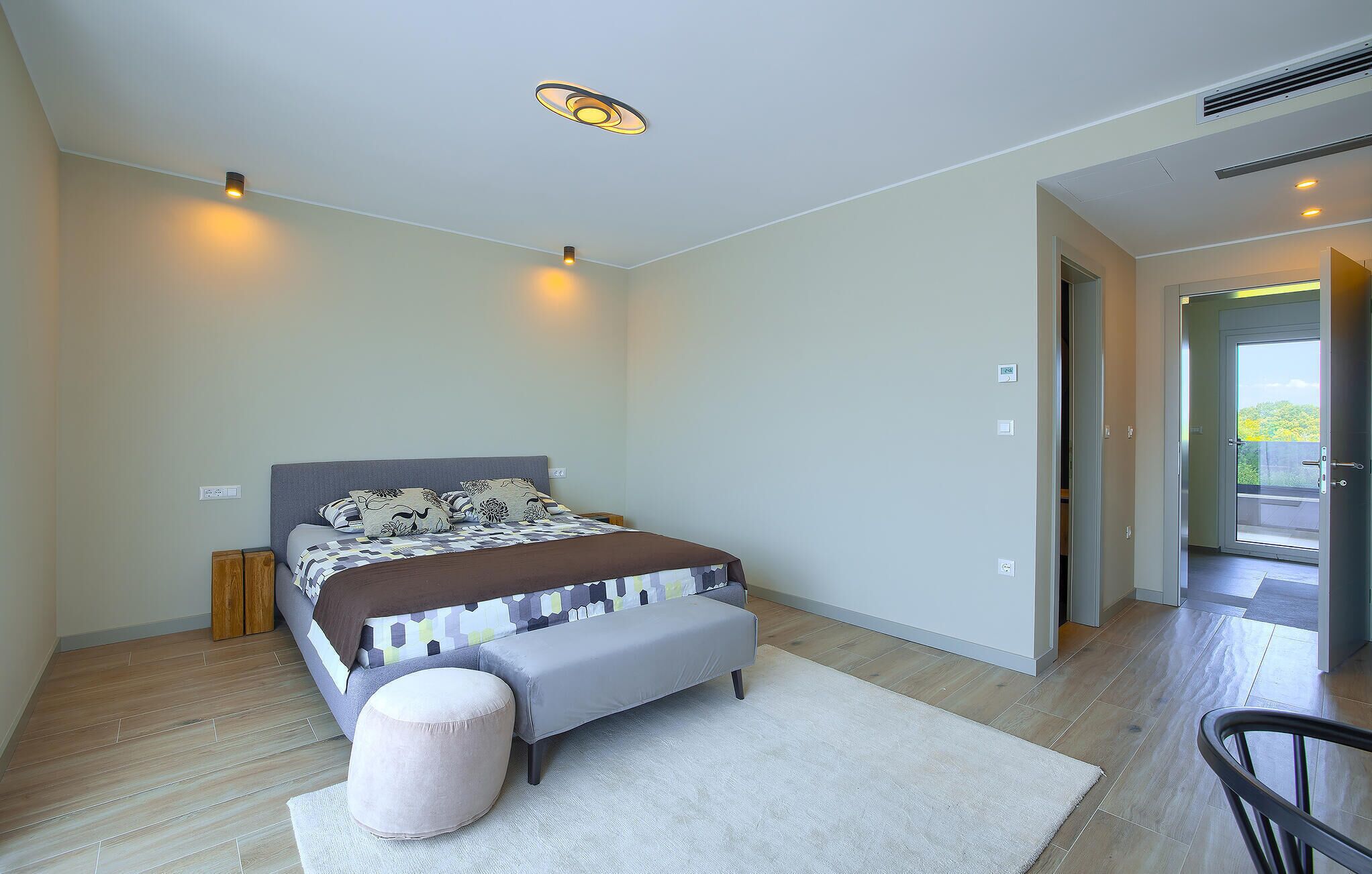 Ein Schlafzimmer mit einem Bett, Nachttischen, einer Bank, einem Teppich und einer Tür, die auf einen Balkon führt.