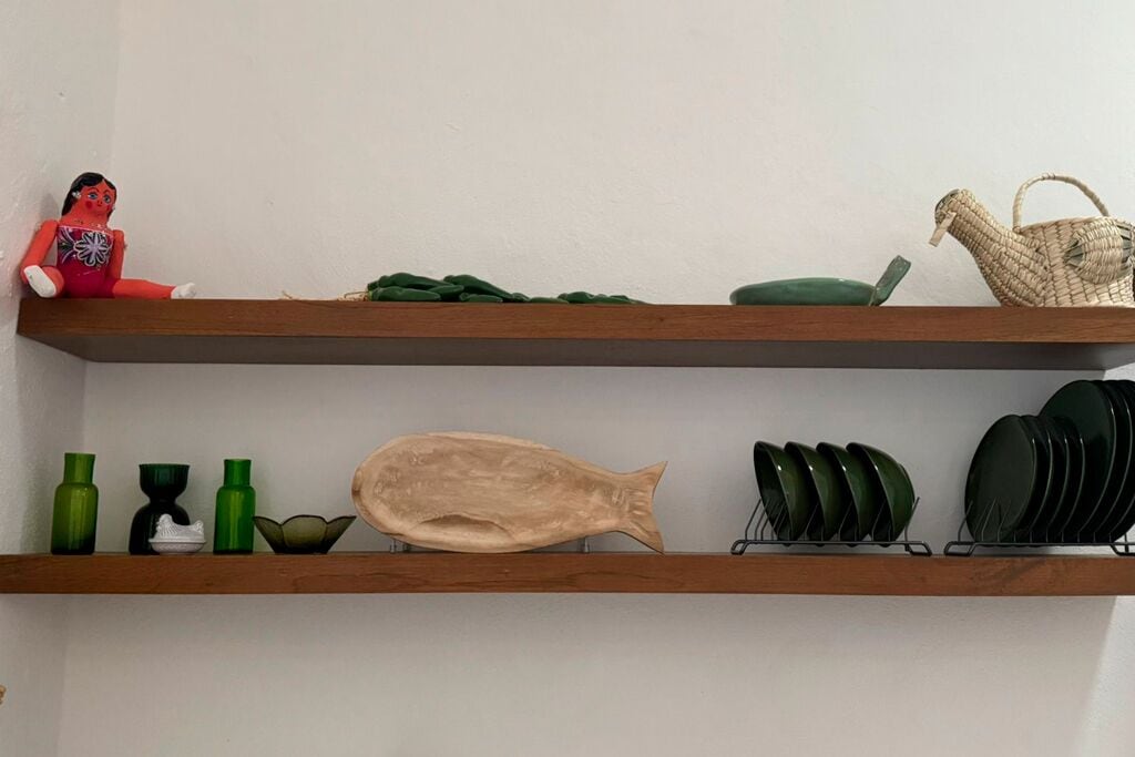 Deux étagères en bois, sur lesquelles sont disposés divers objets, notamment une sculpture de poisson, des bouteilles vertes, un bol blanc et un panier tressé.