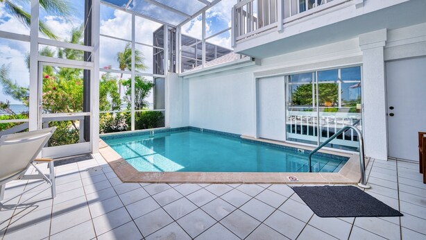 A swimming pool with a glass enclosure, a chair, and a view of the ocean. - Waterfront 2BR with private screened pool (Rum Point)