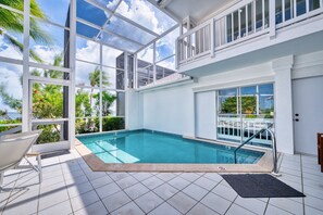 A swimming pool with a glass enclosure, a chair, and a view of the ocean. - Waterfront 2BR with private screened pool (Rum Point)