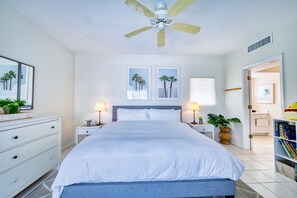 A bedroom with a bed, nightstands, a ceiling fan, a window with blinds, and a bookshelf. - Waterfront 2BR with private screened pool (Rum Point)