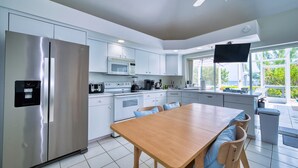 A modern kitchen with a stainless steel refrigerator, a microwave, and a dining area with a wooden table and chairs. - Waterfront 2BR with private screened pool (Rum Point)