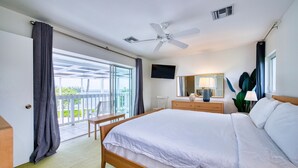 A hotel room with a bed, a television, a ceiling fan, a window with curtains, and a view of the outdoors. - Waterfront 2BR with private screened pool (Rum Point)