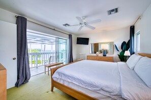 A hotel room with a bed, a television, a ceiling fan, a window with curtains, and a view of the outdoors. - Waterfront 2BR with private screened pool (Rum Point)
