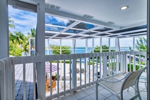 Un balcon avec vue sur la mer, une balustrade blanche et du mobilier d’extérieur.
