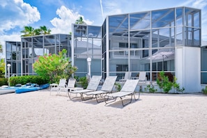 A modern building with large glass windows, outdoor seating, and a clear sky. - Waterfront 2BR with private screened pool (Rum Point)