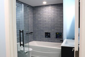 A modern bathroom with a glass shower enclosure, a white bathtub, and a black sink. - Relaxing Coastal Retreat, Elevator, Dog Friendly (Emerald Isle)