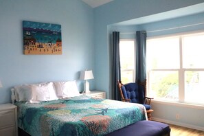 A bedroom with a bed, a chair, a nightstand, a lamp, and a painting on the wall. - Relaxing Coastal Retreat, Elevator, Dog Friendly (Emerald Isle)