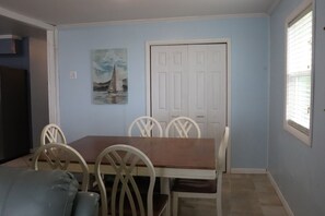A dining area with a table and chairs, a door, and a painting on the wall. - Relaxing Coastal Retreat, Elevator, Dog Friendly (Emerald Isle)