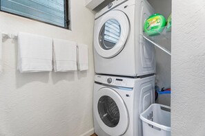 Uma área de lavanderia com máquina de lavar e secadora empilhadas, uma prateleira com detergente e uma cesta.