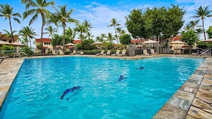 Une piscine où nagent deux personnes, entourée de palmiers et de chaises longues.