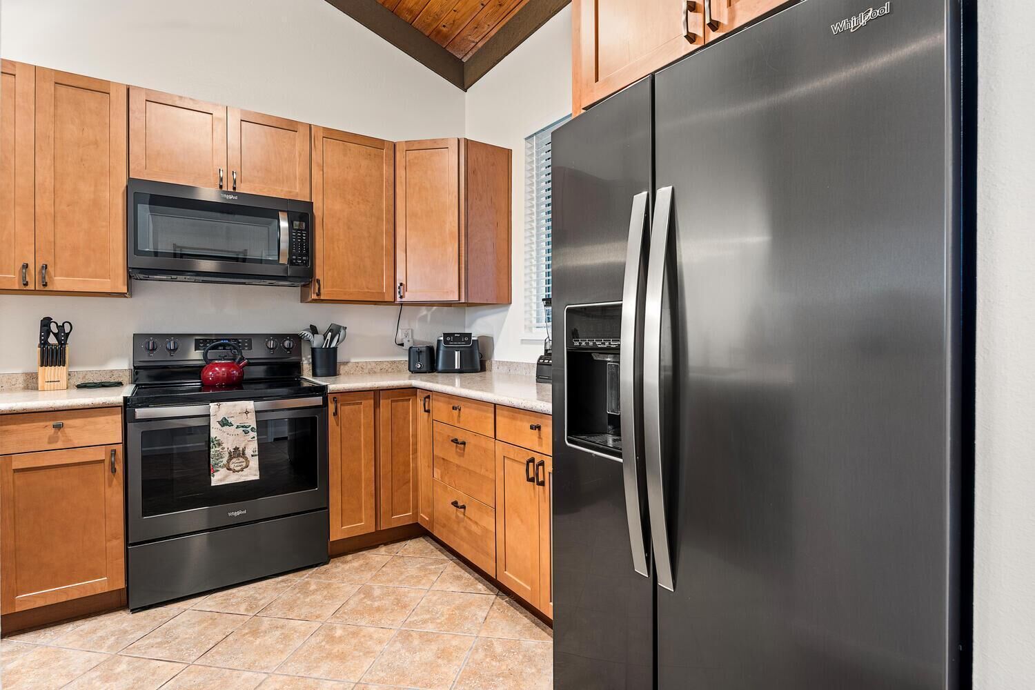 A kitchen with wooden cabinets, a stainless steel refrigerator, a microwave, an oven, and a kettle.