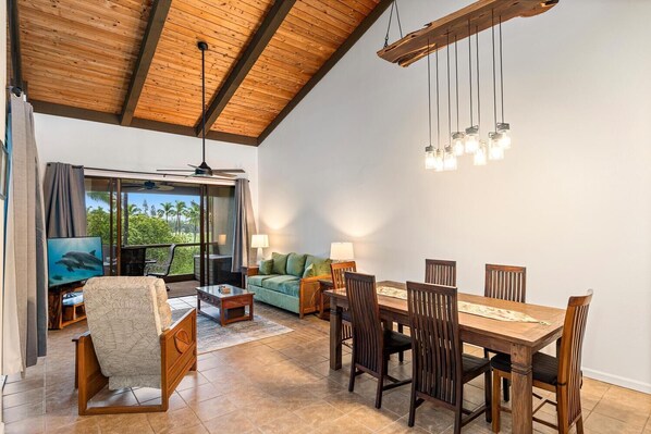 A spacious room with a wooden ceiling, a dining table with chairs, a sofa, a TV, and a view of the outdoors. - Kksr#7-304: Incredibly Private Top Floor Corner! (Kailua-Kona)