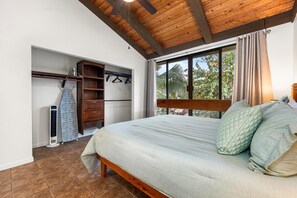 Quarto com cama, vigas de madeira no teto, guarda-roupa e janela com vista para o verde.