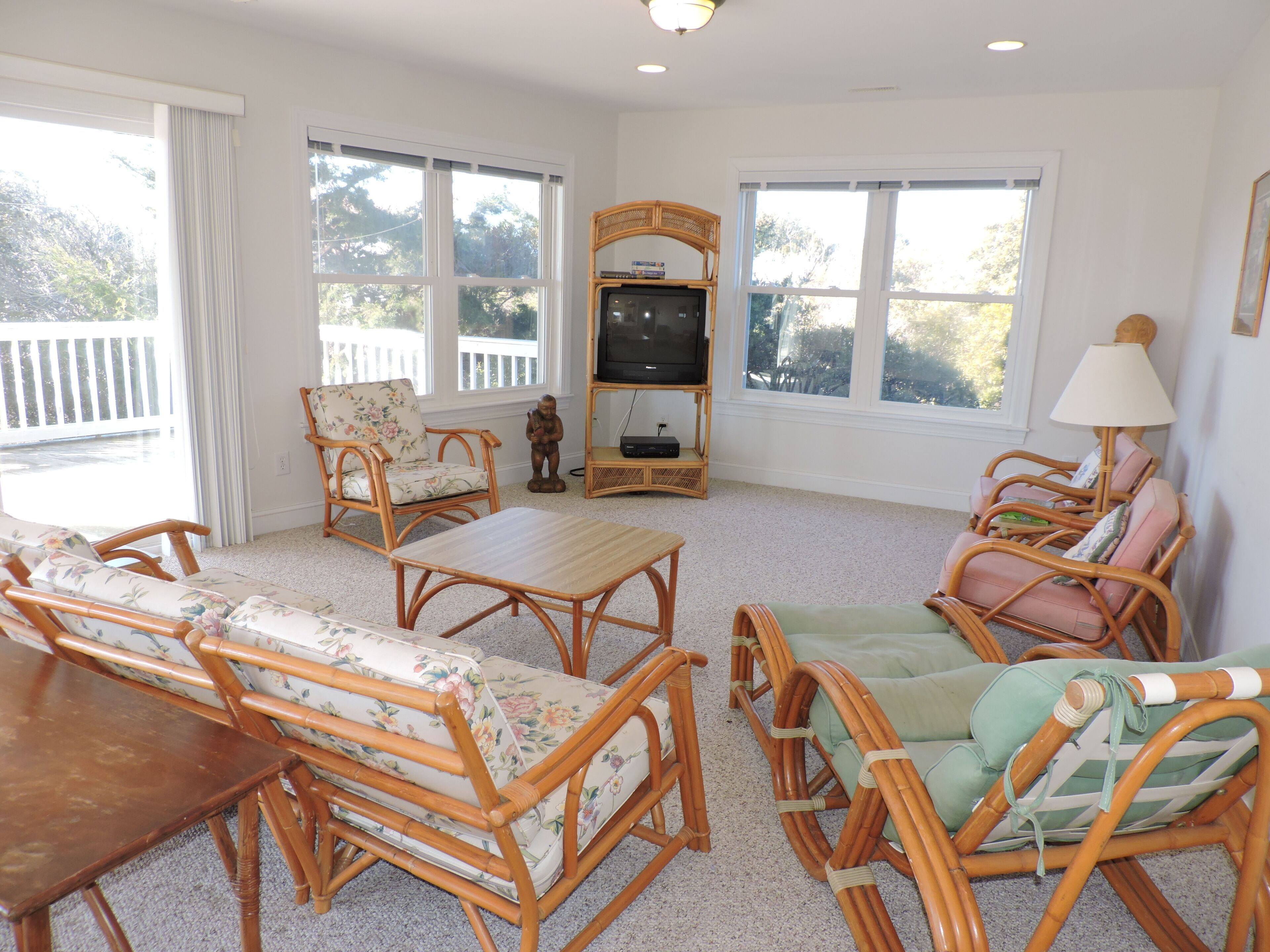 A living room with wicker furniture, a television, and large windows.