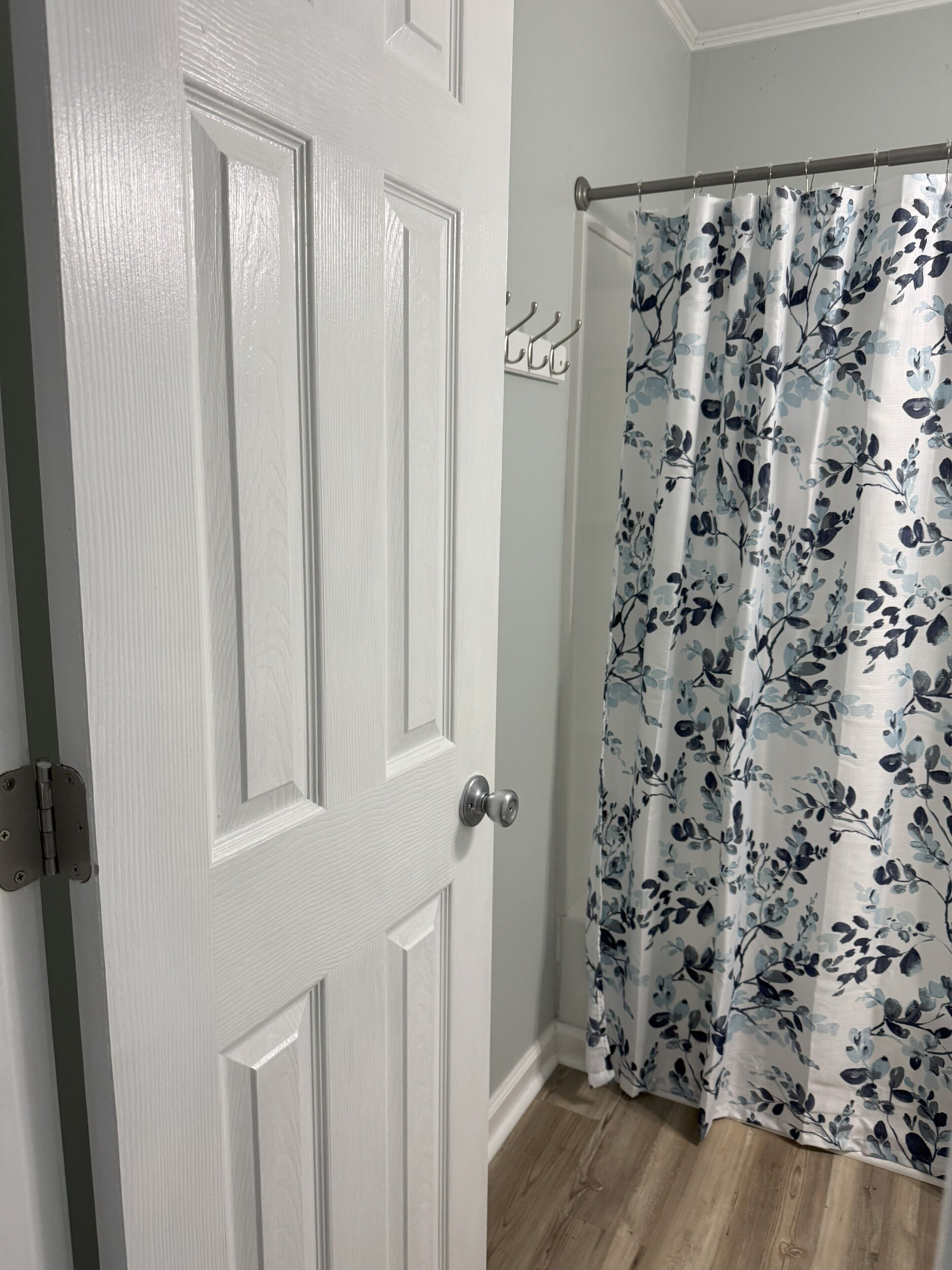 A white door with a silver handle, a shower curtain with a floral pattern, and a wooden floor.
